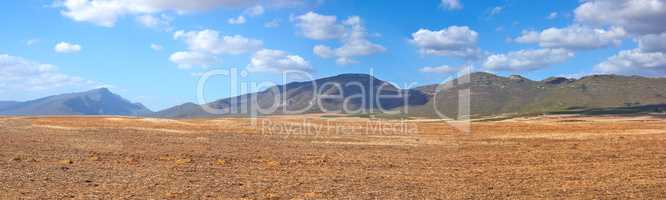 Landscape of harvested farm land on a cloudy day. Empty wheat field against a blue sky. Rural agriculture with dry pasture near mountains. Wide angle of empty dirt country for copy space background.