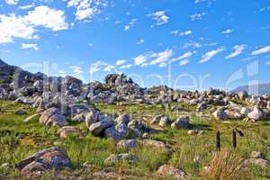 Secluded hiking location for scenic nature. Landscape of rocky mountain with boulders against a blue sky in summer. Green field with rocks and wild grass growing on sunny day outside with copy space