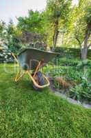 Maintenance equipment on cut fresh green grass in a clean backyard used for gardening, moving plants, vegetations, dry leaves and branches. A wheelbarrow on a lawn in a garden.