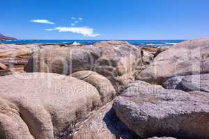 Rocky coastline with the ocean and blue sky with copyspcae in the background. Stunning nature landscape or seascape of rocks. Boulders or big natural stones in the sea with beautiful rough textures