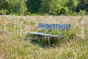 An old wooden bench in an open field outside with a forest in the background. Find a quiet place to enjoy the beauty of nature. The woods can be a peaceful and tranquil place when you need to be alone