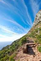 Scenic mountain hiking trail with copy space, rough rocks or stones leading to beautiful view of ocean or sea from the peak. Landscape of rough path with rocks and blue sky in remote nature reserve