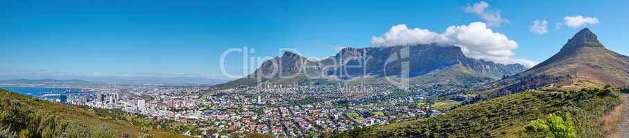 Panoramic landscape of Table mountain and surrounding urban town and a scenic road for traveling along Cape Town, South Africa. A mountain road overlooking the city with a cloudy blue sky in summer