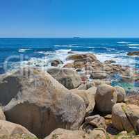 Beautiful seascape beach waves splashing against boulders or big stones in aqua sea water. A summer nature location in South Africa. Rocks in the ocean under a blue sky background with copy space.