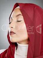 Closeup of a glowing beautiful muslim woman with eyelash extensions isolated against grey background in studio. Young woman wearing a red hijab or headscarf and jewellery. Perfect and flawless skin