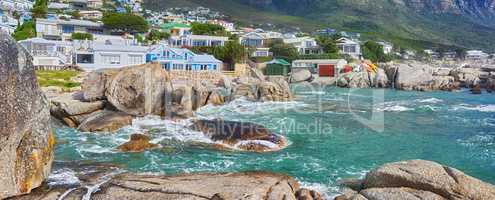 Scenic view of sea, rocks and residential buildings in Camps Bay Beach, Cape Town, South Africa. Tidal ocean waves washing over shoreline rocks and boulders. Overseas travel and tourism destination