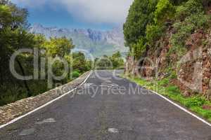 Empty road on the mountains with a cloudy blue sky. Landscape of a countryside roadway for traveling on a mountain pass along a beautiful scenic nature drive with green trees and mountain views