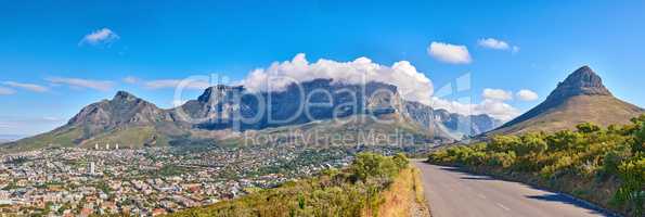 Table Mountain is a hiking destination for tourists and locals surrounded by nature, trees and houses. Scenic road view of clouds resting on the popular tourist attraction in the city Cape Town.