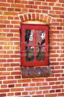 Dirty window in an old red brick house outside. Background of an architectural built structure on an exterior wall with red wooden windowpanes shut close. Historic building in a traditional town