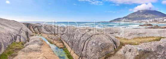 Rocky coastline with the ocean and mountains in the background. Stunning nature landscape or seascape of rocks. Boulders or big natural stones in the sea with beautiful rough textures and copy space