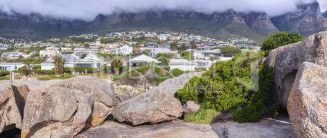 Rocks and boulders against a majestic mountain and cityscape background with lush green plants and coulds. Remote and quiet landscape on a cliff with stones to enoy a urban view with private homes