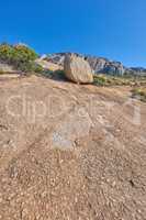 Mountainside with large boulders and lush plants with copy space. Indigenous dry fynbos and wild grass growing on a rocky hill in summer warm weather. Quiet nature scene with tropical weather