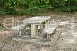 A bench made of concrete and ceramics outside in a luscious green forest during summer or spring. A quiet place to enjoy nature and the view the woods have to offer. A tranquil place amongst the trees