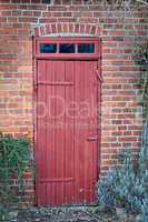 An old, large, red wooden door in a face brick building, most likely a house in a residential district. The entrance way to a house or home. When opportunity knocks, you answer. A vintage residence