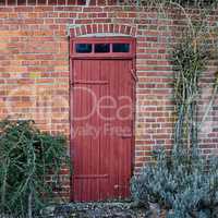 An old, large, red wooden door in a face brick building, most likely a house in a residential district. The entrance way to a house or home. When opportunity knocks, you answer. A vintage residence