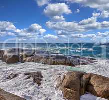 Rocks in the ocean under a blue cloudy sky with copy space. Scenic landscape of beach waves washing over boulders or big stones in the sea at a popular summer location in Cape Town, South Africa