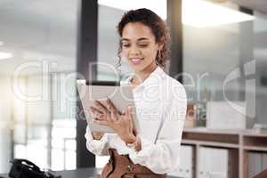 My plan is in motion. a young businesswoman using a digital tablet while standing in her office.