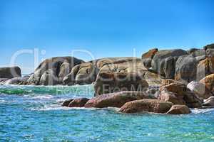 Boulders or big rocks in a calm ocean against a clear blue sky background with copy space. Beautiful seascape across the horizon and rocky coast. Perfect destination for a summer holiday or getaway