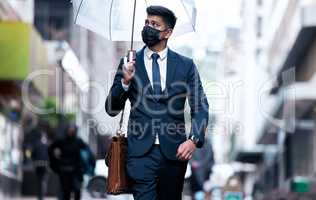 Paving his path in the new world. Portrait of a young businessman wearing a face mask and holding an umbrella on a rainy day in the city.