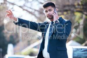Catching a ride to success. a young businessman talking on a cellphone while hailing a cab in the city.