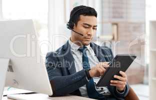 Lets tick that off our list. a young male call center agent using a computer and digital tablet in an office at work.