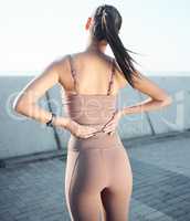 A proper warm-up before running can help prevent back pain. Rearview shot of a sporty young woman experiencing back pain while exercising outdoors.