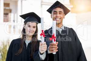 We put in tons of effort to achieve this. Portrait of a young man and woman celebrating with their diplomas on graduation day.