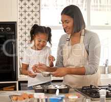 You have to do it slowly. an adorable little girl baking with her mom at home.