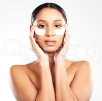 Beat back the years. Studio portrait of an attractive young woman using under eye patches against a grey background.