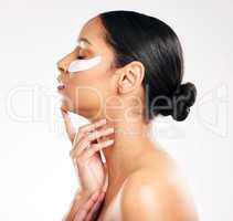 Being wrinkle-free is no accident. Studio shot of an attractive young woman using under eye patches against a grey background.