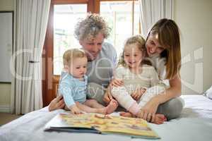 Look at the picture, listen for the sound. a young family happily bonding while reading a book together in bed at home.