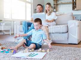 A supportive family is what builds a home. a boy playing with his toys while his parents sit on the couch and use a laptop at home.