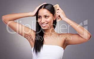 Brushing the scalp stimulates hair growth. an attractive young woman standing alone in the studio and combing her hair.