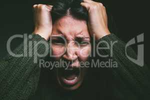 Is it all in your head. Studio shot of a young woman experiencing mental anguish and screaming against a black background.