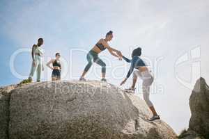 No one can do it alone. a woman helping her friend climb a boulder during a workout.