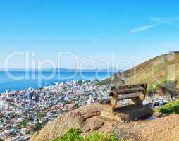 Public bench on a cliff looking at the city and sea in summer. Scenic and landscape view of a seat on a mountain to relax and enjoy the view of the town. Peaceful, quiet, and secluded natural area