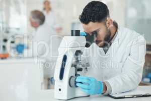 The cure takes time to perfect. a young scientist using a microscope in a lab.