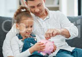 Teaching her the value of money. a father teaching his daughter to save in a piggybank.