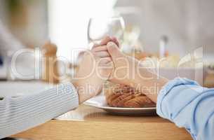 Families that pray together, enter heaven together. two unrecognizable people holding hands at the dinner table at home.