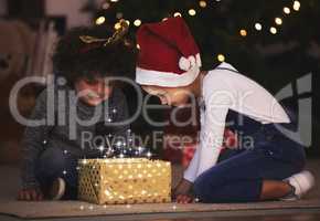 Unlock the magic of Christmas. two little siblings opening up a gift together at home.