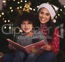 Mom always chooses the best stories. a young mother and son reading a book during Christmas time at home.