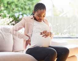 Being pregnant can be a bit uncomfortable at times. an attractive young mother to be looking uncomfortable while sitting on the sofa at home.