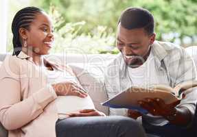 Story time. a handsome young man reading a book to pregnant wifes belly while sitting on the sofa at home.