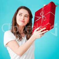 I wonder what it could be. Studio shot of an attractive young woman trying to figure out what her gift is against a blue background.