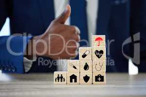 Dont just be sure, be insured. an unrecognisable businessman assembling wooden blocks with insurance related symbols on them and showing thumbs up.