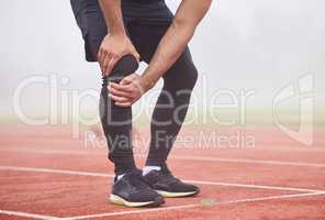 Looks like his race is run. an unrecognizable male athlete holding his knee in pain while standing out on the track.