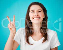 Peace, love and positivity. Studio portrait of an attractive young woman showing the peace sign to the camera against a blue background.