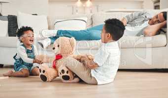 Dad needs a break. two siblings fighting over a teddy on the floor while their dad sleeps on the couch at home.