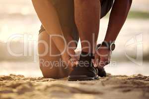 I wont allow myself to stumble. Closeup shot of an unrecognisable man tying his laces while exercising at the beach.