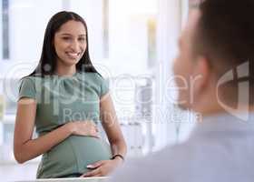 I have a few more months to go. a young pregnant businesswoman sitting with a colleague in the office and holding her belly.